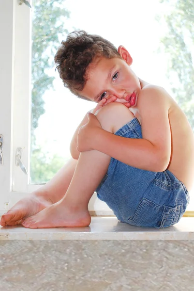 Sitting on the windowsill sad resentful boy — Stock Photo, Image