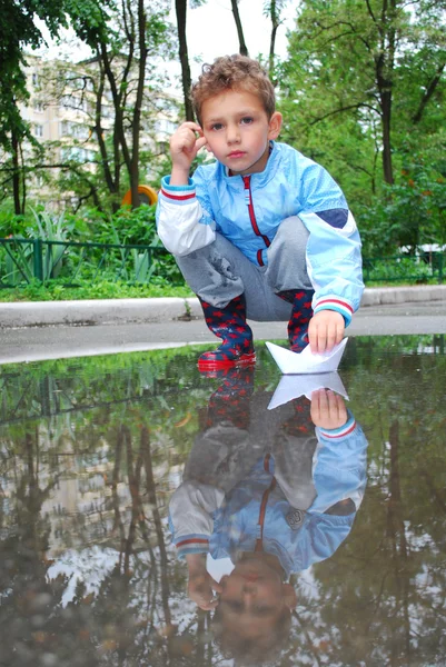 Мальчик в бассейне играет с бумажными лодками — стоковое фото