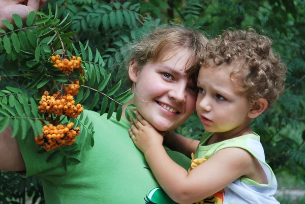 En el bosque cerca de un árbol con rowan, madre sostiene a su hijo en él —  Fotos de Stock