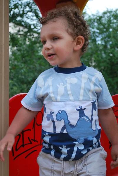 Pequeno, menino de cabelos encaracolados brincando no playground . — Fotografia de Stock