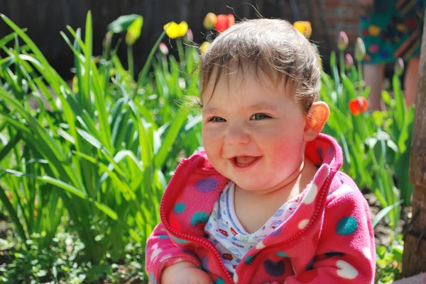 Il villaggio si siede vicino ai tulipani nel giardino, una bambina un — Foto Stock