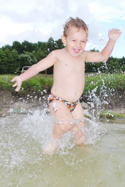 Kleiner Junge läuft in den Fluss und planscht überall. — Stockfoto