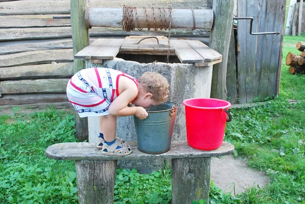 Na aldeia perto do poço um menino bebe água de um b — Fotografia de Stock