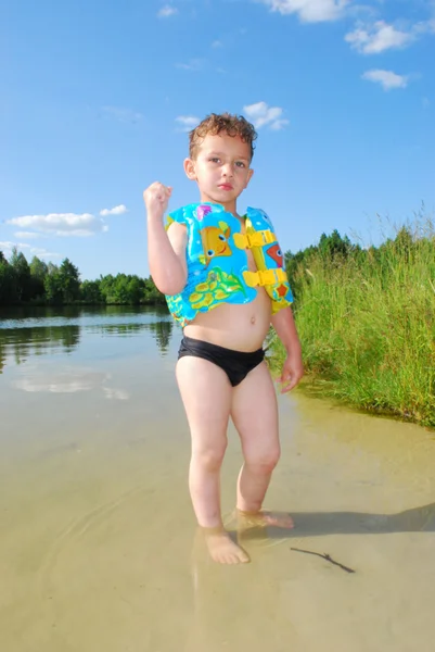 Menino bonito fica em um lago, vestindo calções de banho e um v — Fotografia de Stock