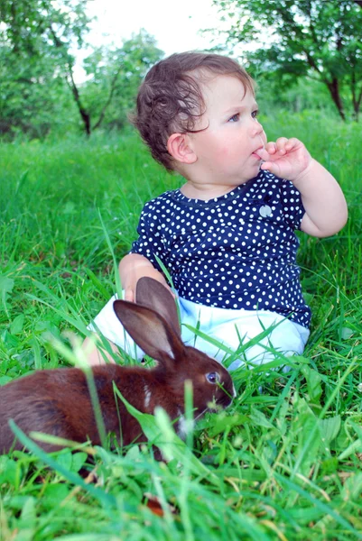 Sitting on the grass a little girl, and by her black rabbit. — Stock Photo, Image