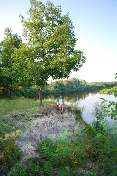 Im Sommer, in der Nähe des Flusses, auf einer Klippe, sitzt ein Mann mit seinem — Stockfoto