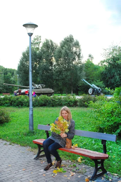 Im Park sitzt das Mädchen auf der Bank und hält einen Strauß Gelbtöne in der Hand — Stockfoto