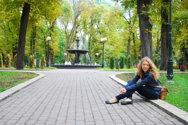 縁石に座っている女の子の泉の近くの公園で. — ストック写真