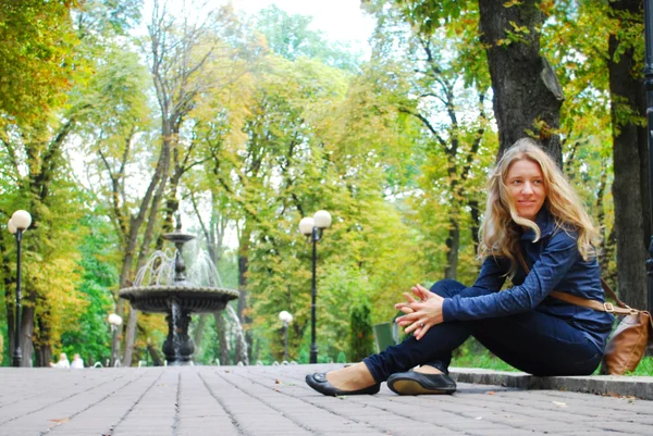 In the park near the fountain, girl sits on the curb. — Stock Photo, Image