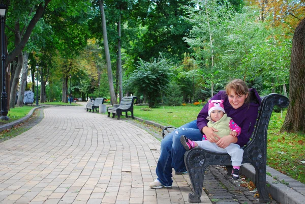 En el parque, mamá sentada en el banco y sosteniendo a un bebé daughte — Foto de Stock