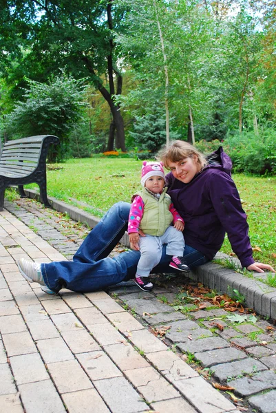 In the park, mom sitting on the curb and holding a baby daughter — Stock Photo, Image