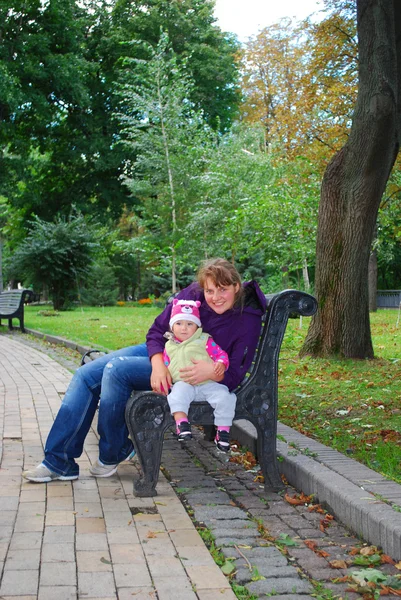 En el parque, mamá sentada en el banco y sosteniendo a un bebé daughte —  Fotos de Stock