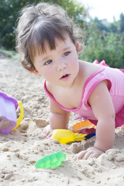 Na praia na areia menina senta-se e brinca com um dinheirinho — Fotografia de Stock