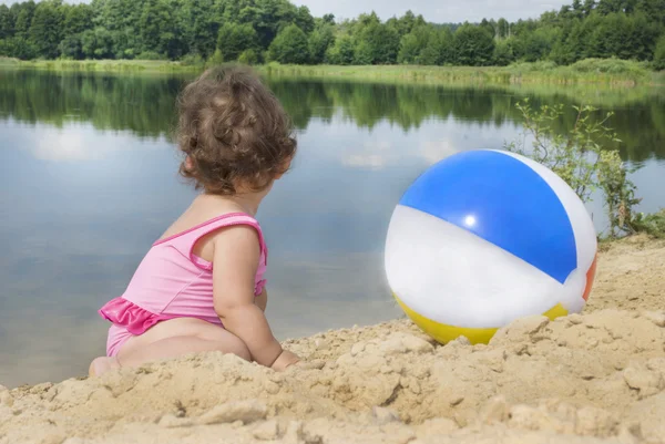 On the beach near the lake in the sand little girl playing with — Stock Photo, Image