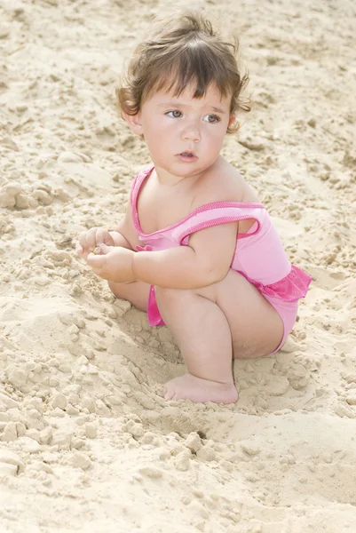 На пляже в песке маленькая девочка сидит и играет — стоковое фото