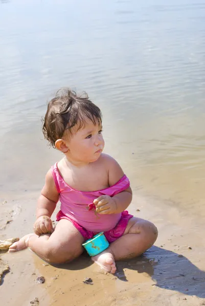 On the beach near the lake in the sand little girl playing with — Stock Photo, Image