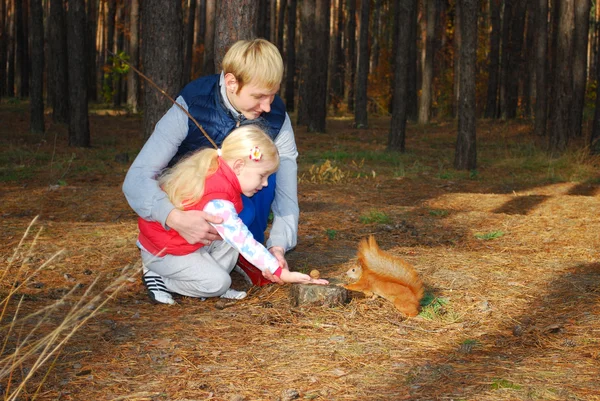 Im Kiefernwald füttern Vater und Tochter ein Eichhörnchen. — Stockfoto