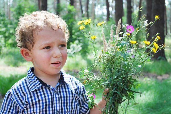 Upprörd liten pojke med en bukett blommor — Stockfoto