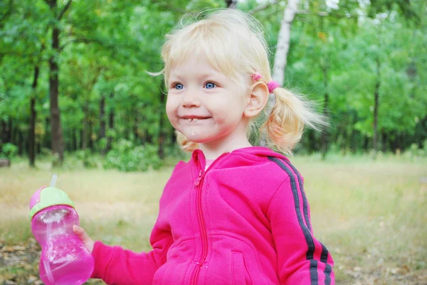 A little blue-eyed blonde girl holding a bottle of water with e — Stock Photo, Image