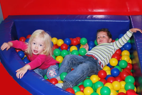 Pojke till en flicka som leker i poolen med färgglada bollar. — Stockfoto