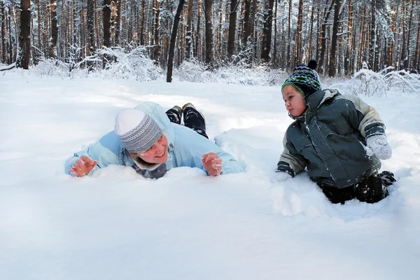 Vintern mamma med sin son njuta av ligger på snön i skogen — Stockfoto