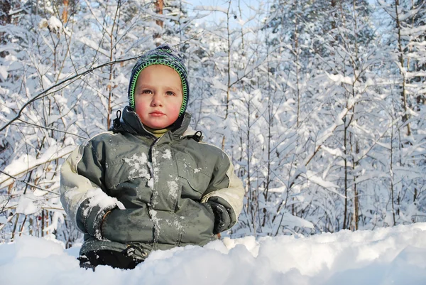 På snön i vinter sitter skog en liten pojke. — Stockfoto