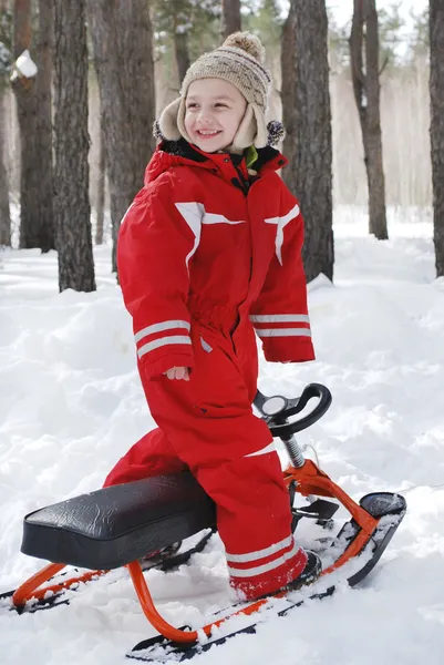 Invierno en el bosque se encuentra un niño en moto de nieve y sonriendo . — Foto de Stock