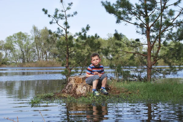 Chlapče, sedí na pařezu nedaleko břehů řeky publikoval moh — Stock fotografie