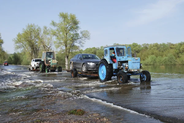 Überschwemmungen, überflutete Straße Traktor trägt Autos. — Stockfoto