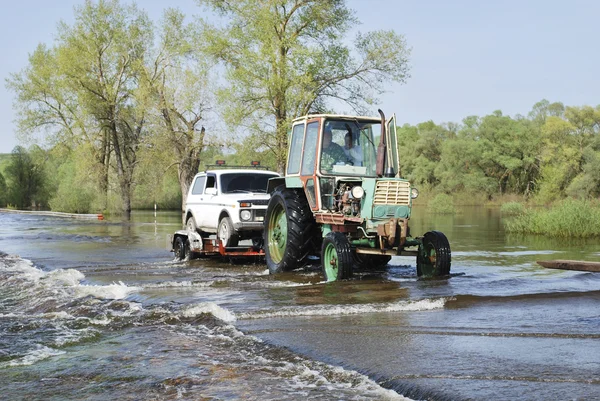 Überschwemmungen, überflutete Straße Traktor trägt Autos. — Stockfoto