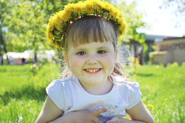 Kleine meisjes zitten in een veld in een krans van paardebloemen. — Stockfoto