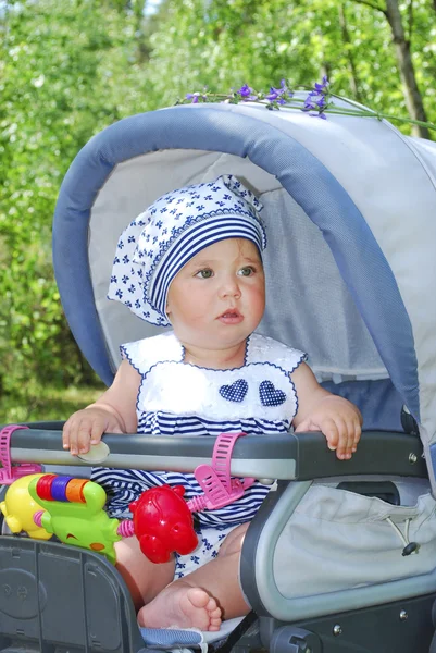 I sommar, söt liten flicka sitter i barnvagn och ler. — Stockfoto