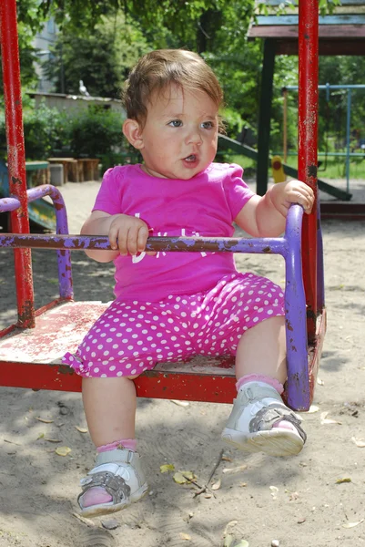 Маленькая девочка сидит на качелях на детской площадке — стоковое фото
