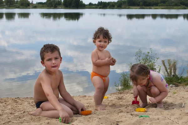 Malé děti si hrají na pláži nedaleko jezera. — Stock fotografie