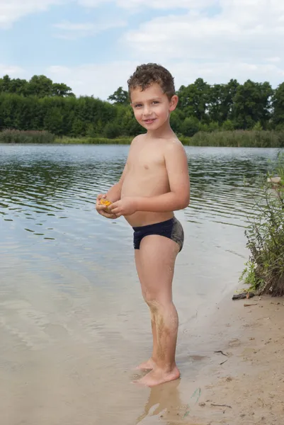 Letni chłopiec stoi na piasku w pobliżu jeziora. — Zdjęcie stockowe