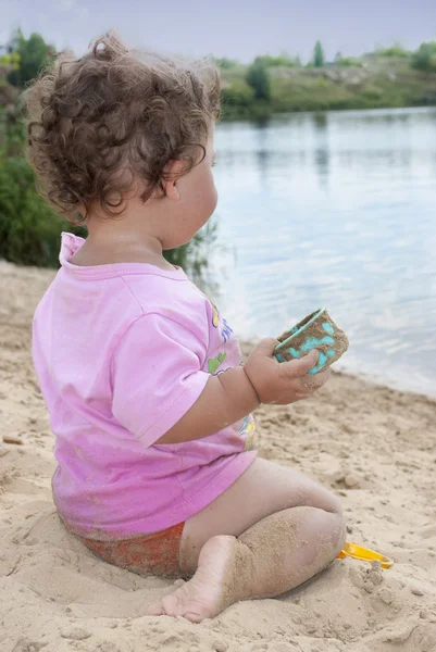 Op het strand in de buurt van het meer in het zand meisje spelen met — Stockfoto