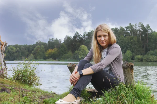 Meisje zittend op de oever van het meer. — Stockfoto