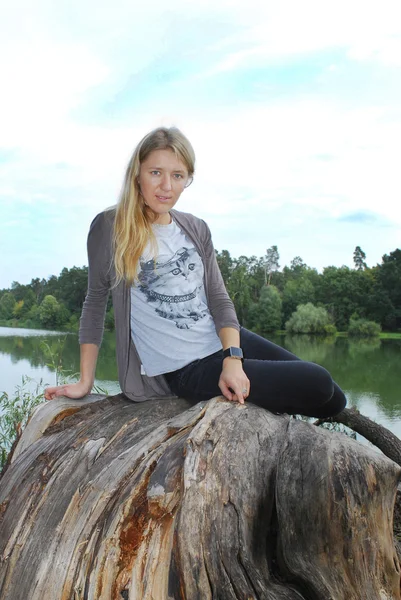Chica sentada en la orilla del lago en el árbol . — Foto de Stock