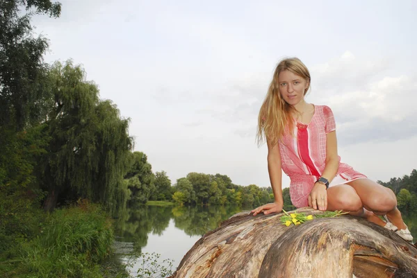 Meisje, zittend op de oever van het meer op de boom. — Stockfoto