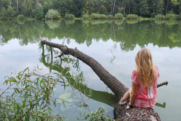 Dziewczyna siedzi na brzegu jeziora na drzewie. — Zdjęcie stockowe