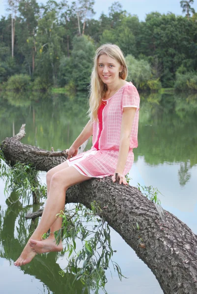 Flicka sitter på stranden av sjön på trädet. — Stockfoto