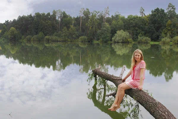 Dívka sedící na břehu jezera na stromě. — Stock fotografie