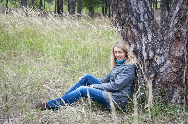 Dívka sedící ve vysoké trávě u borovice. — Stock fotografie