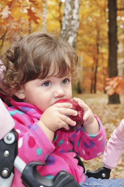 In the forest a little curly-haired girl eats red apple — Stock Photo, Image