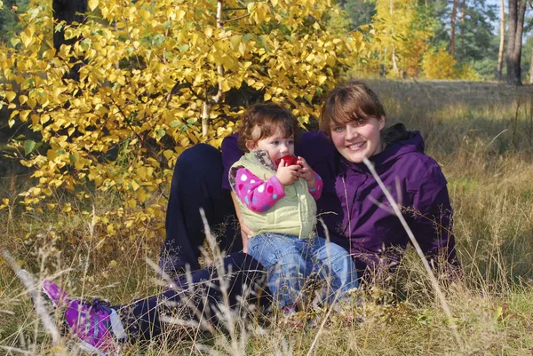 Mom with her daughter  sittingt on grass in autumn forest. — Stock Photo, Image