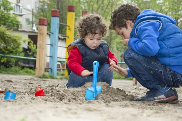 Brother and sister playing in the sand on the playground. — Stock Photo, Image