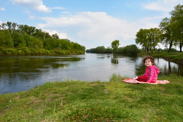川の近くに座っている小さな女の子. — ストック写真