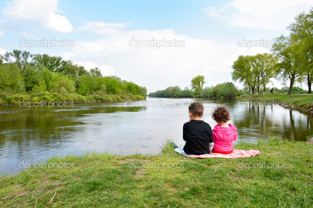 Brother and little sister sitting on the bank of the river.