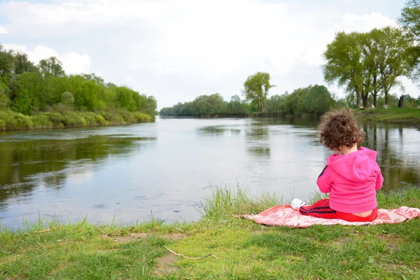 Klein meisje zitten in de buurt van de rivier. — Stockfoto
