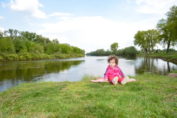 Klein meisje zitten in de buurt van de rivier. — Stockfoto